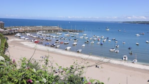 Un port de plaisance situé sur la côte, où de nombreux bateaux sont amarrés, une plage de sable et une jetée en pierre qui s’avance dans l’eau.