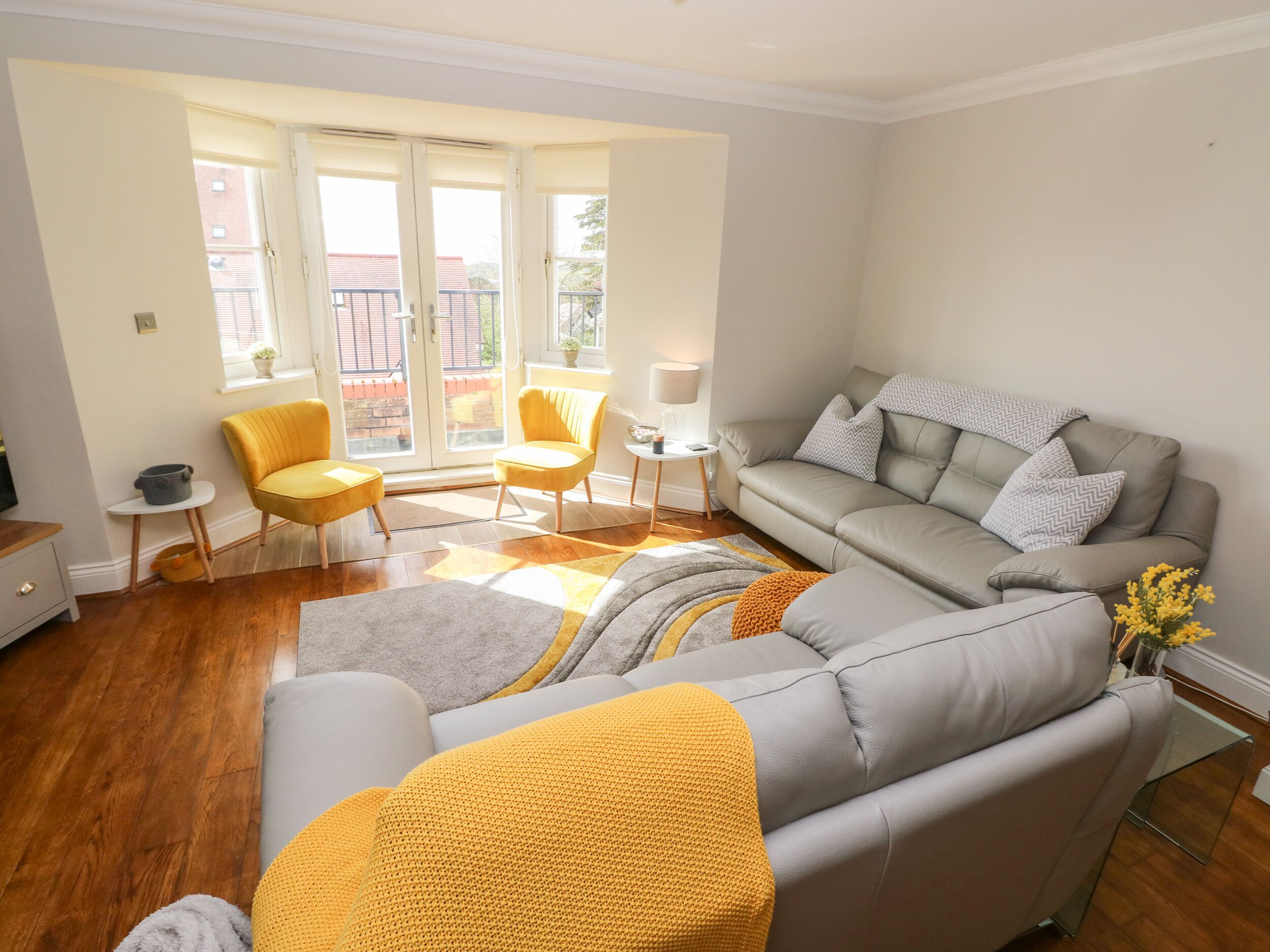 A modern living room with a grey sofa, yellow armchairs, and a glass coffee table.
