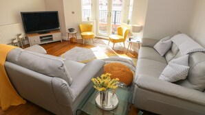 Un salon moderne avec un canapé, un fauteuil, une table basse en verre et un téléviseur.