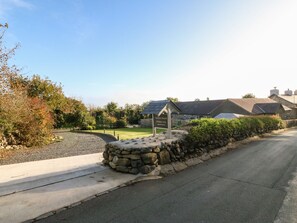 A stone wall, a sign for 'Tyndyn Sianel Holiday Lets', and a building with a sloped roof. - Tyddyn Sianel - Celyn (Criccieth)