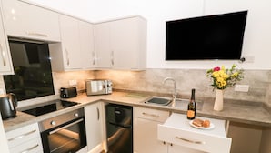 Una cocina moderna con armarios blancos, horno empotrado, microondas, tostadora, lavamanos y un televisor de pantalla plana montado sobre la encimera.