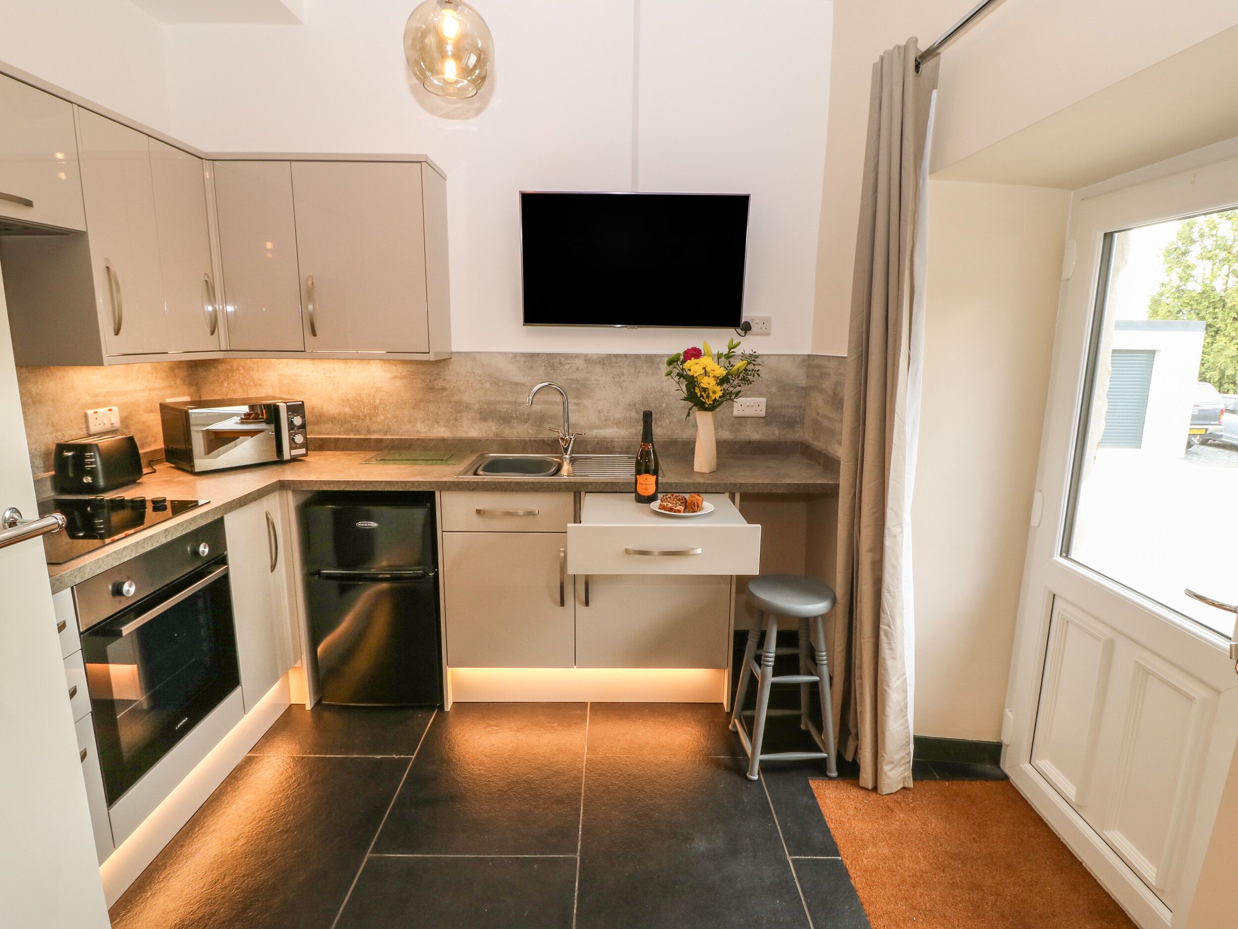 A compact kitchen with modern appliances, a flat-screen TV, and a small dining area.