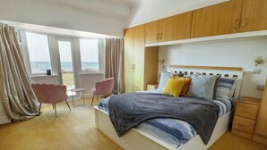 Un dormitorio con cama, mesitas de noche, una silla y vistas al mar a través de grandes ventanales.