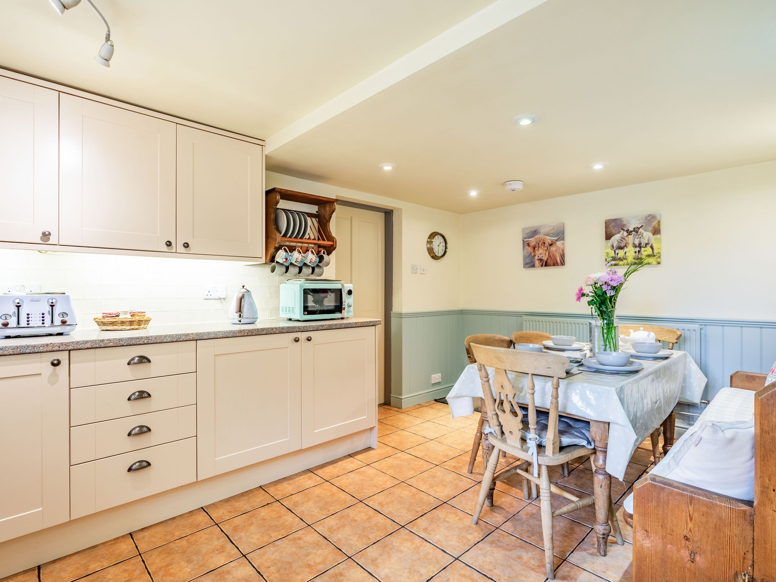 A kitchen with white cabinets, a microwave, and a toaster. There is a dining table with chairs and a vase of flowers.