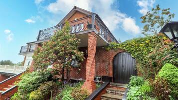 A brick house with a balcony, a black door, and a garden with various plants.