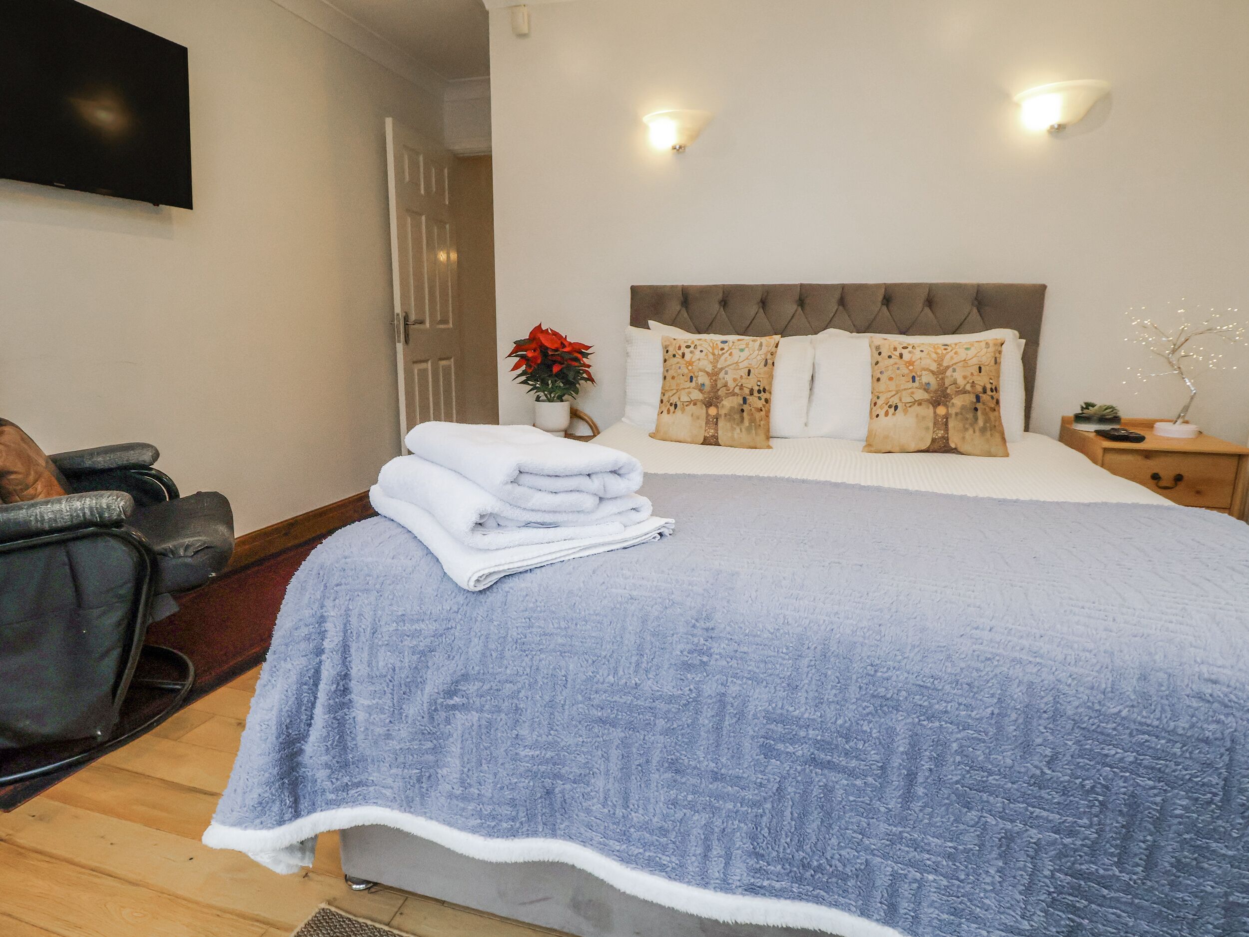 A neatly made bed with a grey duvet, a bedside table with a lamp, and a wall-mounted TV.