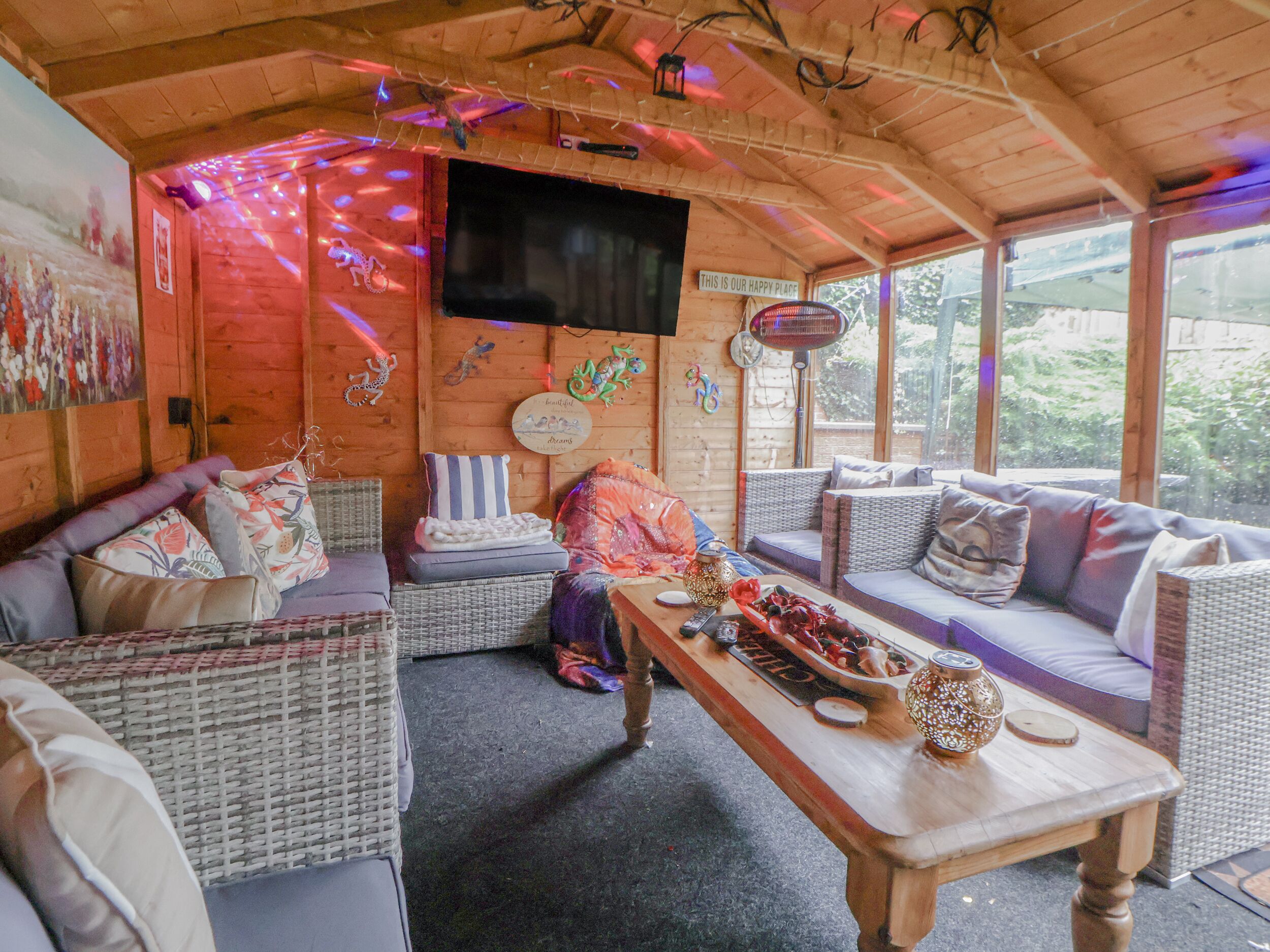 A cozy cabin interior with wicker furniture, a wooden table, and a TV mounted on the wall.