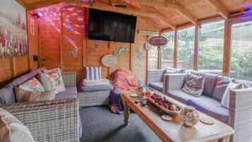 A cozy cabin interior with wicker furniture, a wooden table, and a TV mounted on the wall.