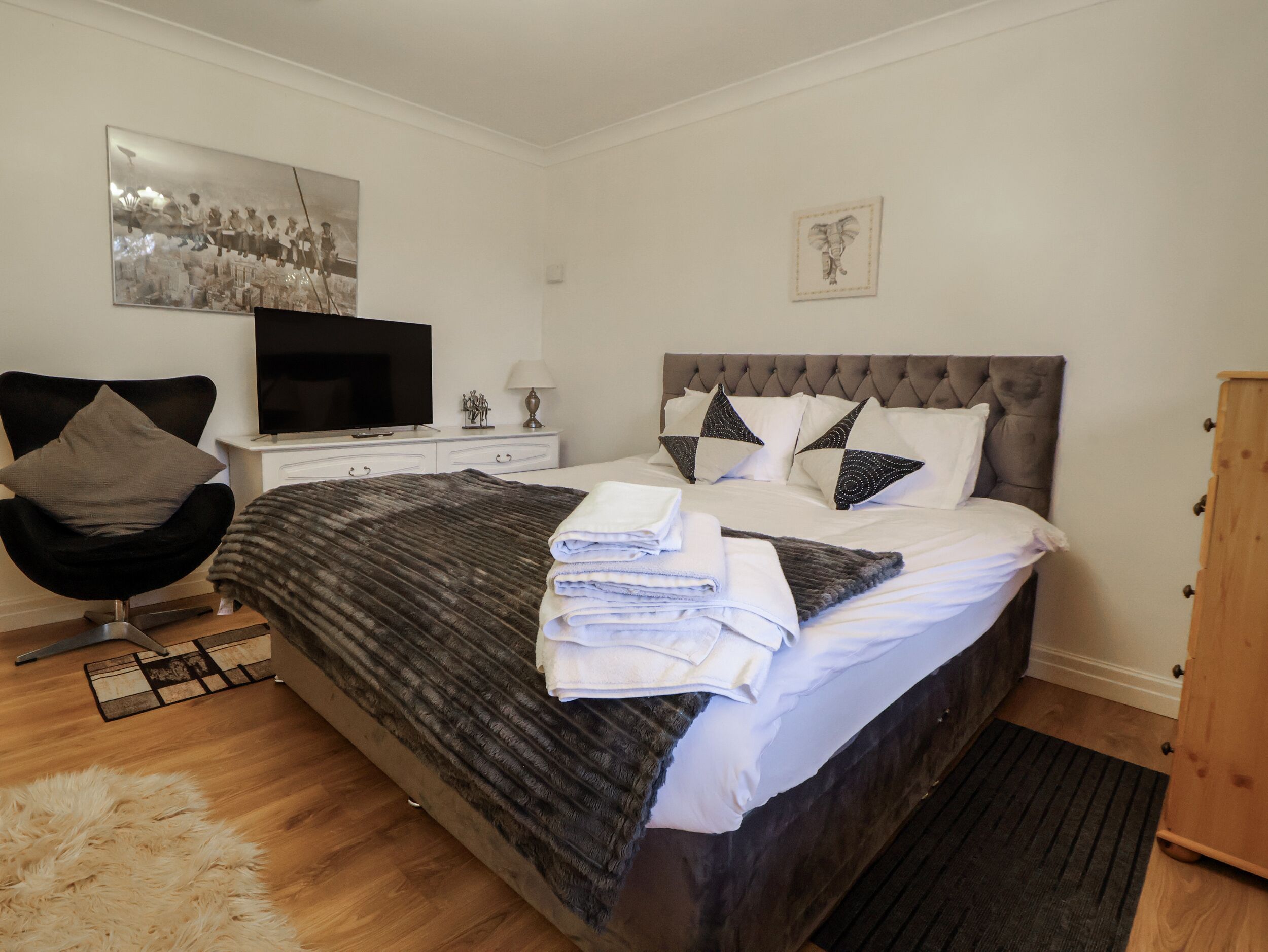 Een moderne slaapkamer met een groot bed, een flatscreen televisie, een stoel en een houten kast.