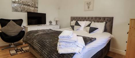 Een moderne slaapkamer met een groot bed, een flatscreen televisie, een stoel en een houten kast.