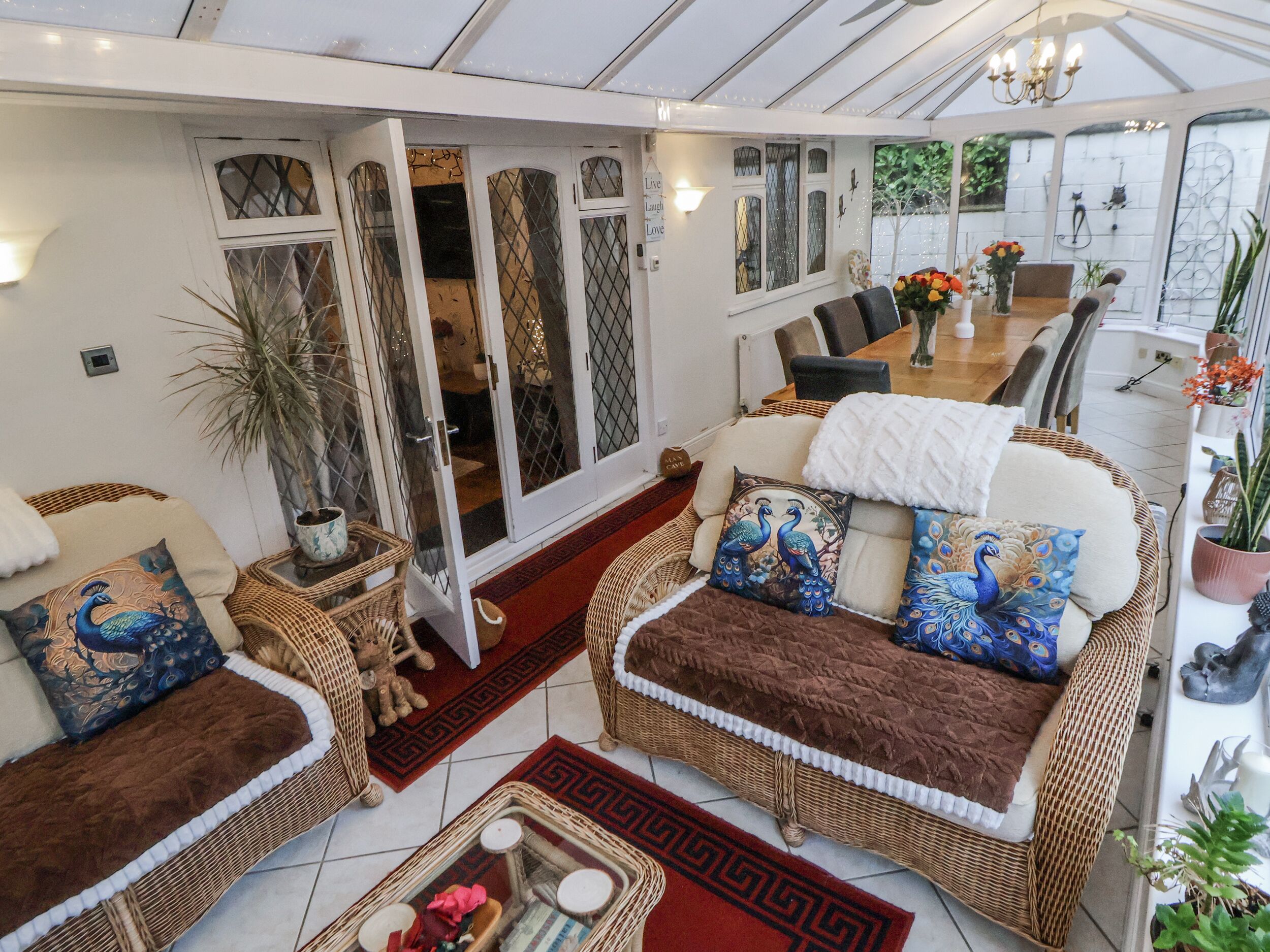A cozy living area with wicker furniture, peacock pillows, and a dining table with chairs.