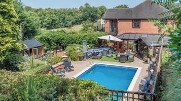 A backyard with a swimming pool, outdoor furniture, and a brick house.