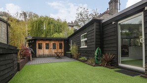 Een modern huis met een houten terras, kunstgras en een tuin.