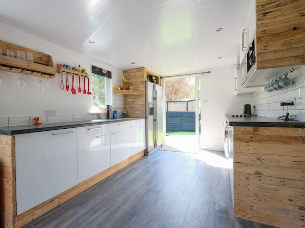 A modern kitchen with white cabinets, wooden accents, and a large island. - By The Beach (Torpoint)