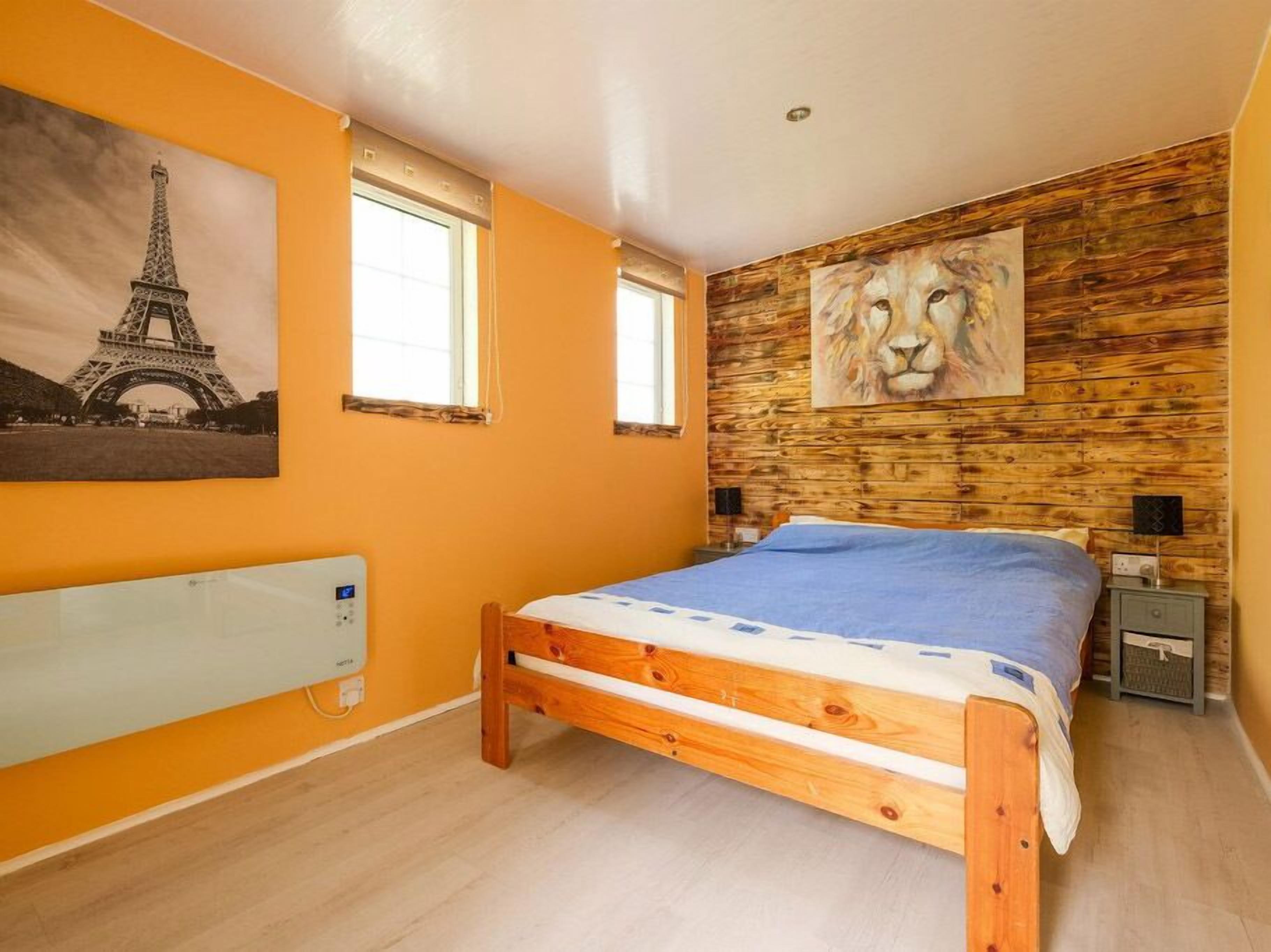 Una camera da letto con un letto di legno, un termosifone, un quadro della Torre Eiffel e un quadro raffigurante un leone, oltre ad una finestra.