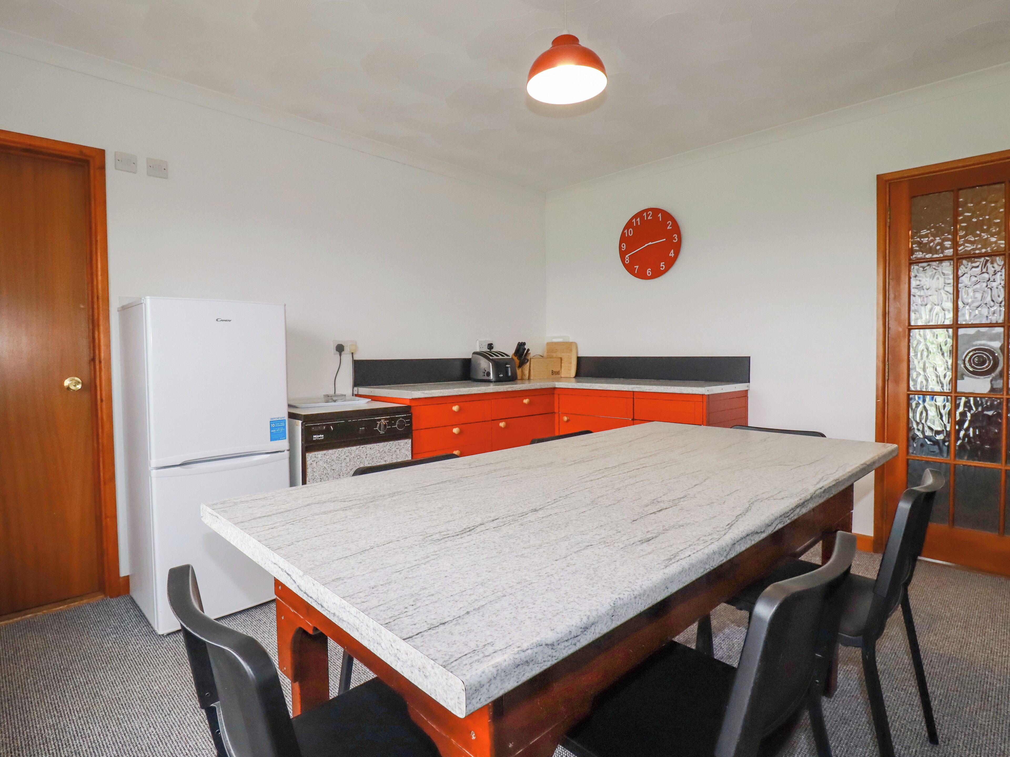 Una cocina compacta con encimera de mármol, un refrigerador, un tostador y un reloj en la pared.