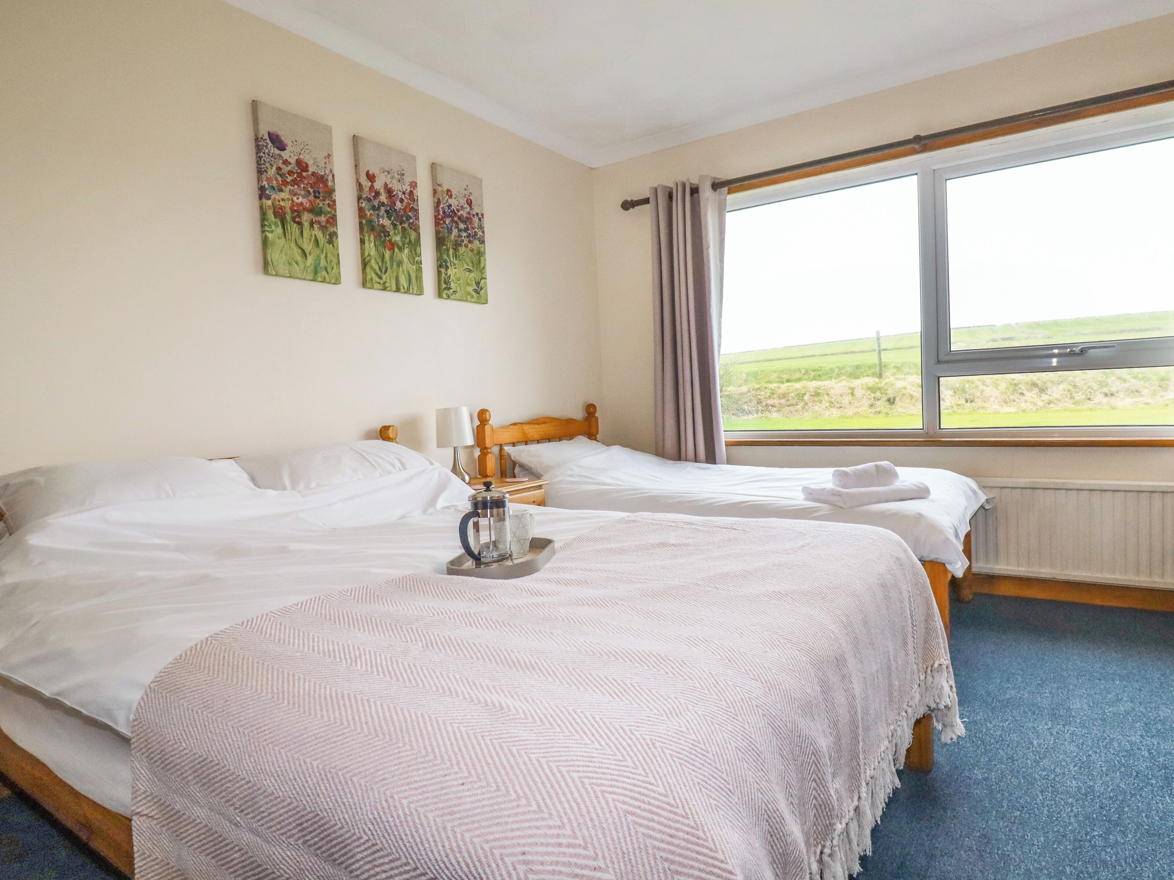 A hotel room with two beds, a coffee maker on the left bed, and a window with a view of the countryside.