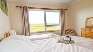 Une chambre d’hôtel avec un lit, une fenêtre avec des rideaux, une commode, un miroir et un plateau avec une cafetière et une tasse.