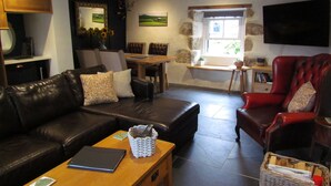 A living room with a leather sofa, a red armchair, a wooden coffee table, and a dining area with a table and chairs. - Trenwith Bridge Cottage (St Ives)
