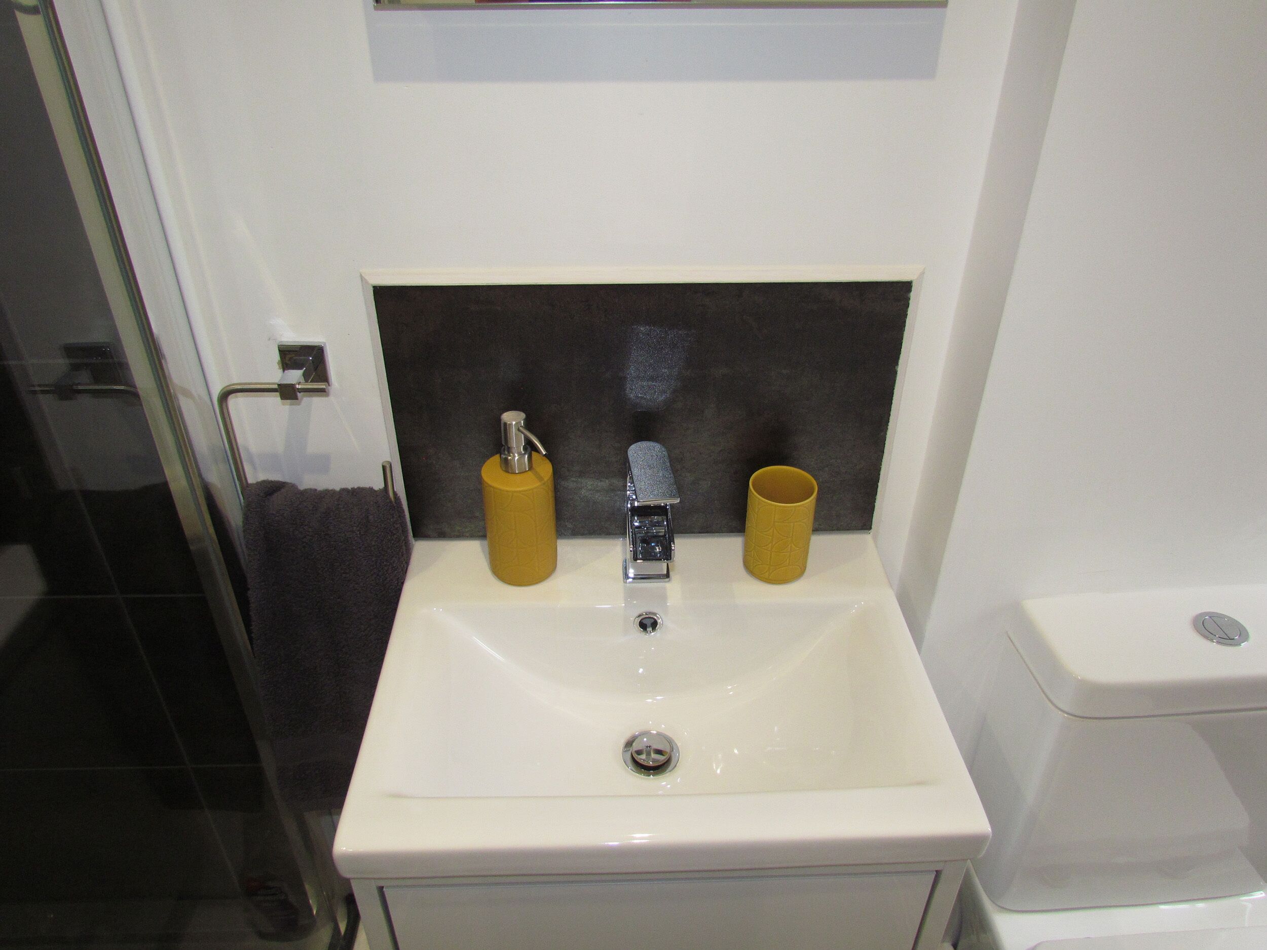 A bathroom with a white sink, a mirror, a towel rack, and two yellow dispensers.
