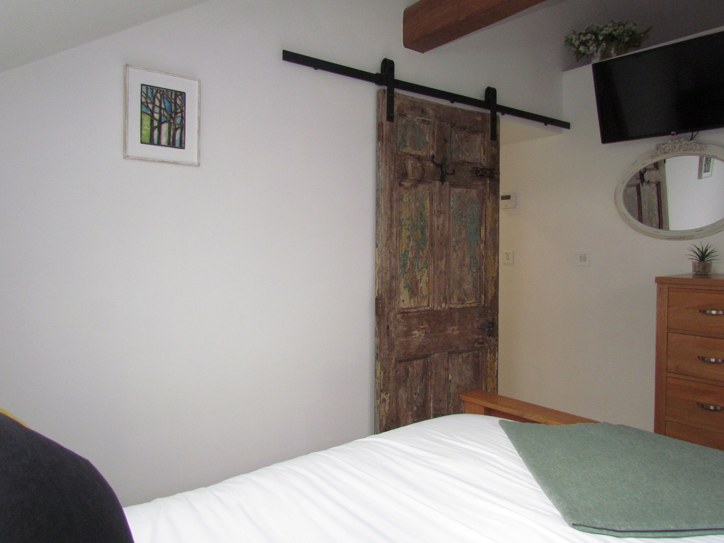 Een slaapkamer met een bed, een houten kledingkast, een aan de muur bevestigde televisie en een ingelijste foto.