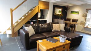 A modern living room with a brown leather sofa, wooden coffee table, and a staircase. - Trenwith Bridge Cottage (St Ives)