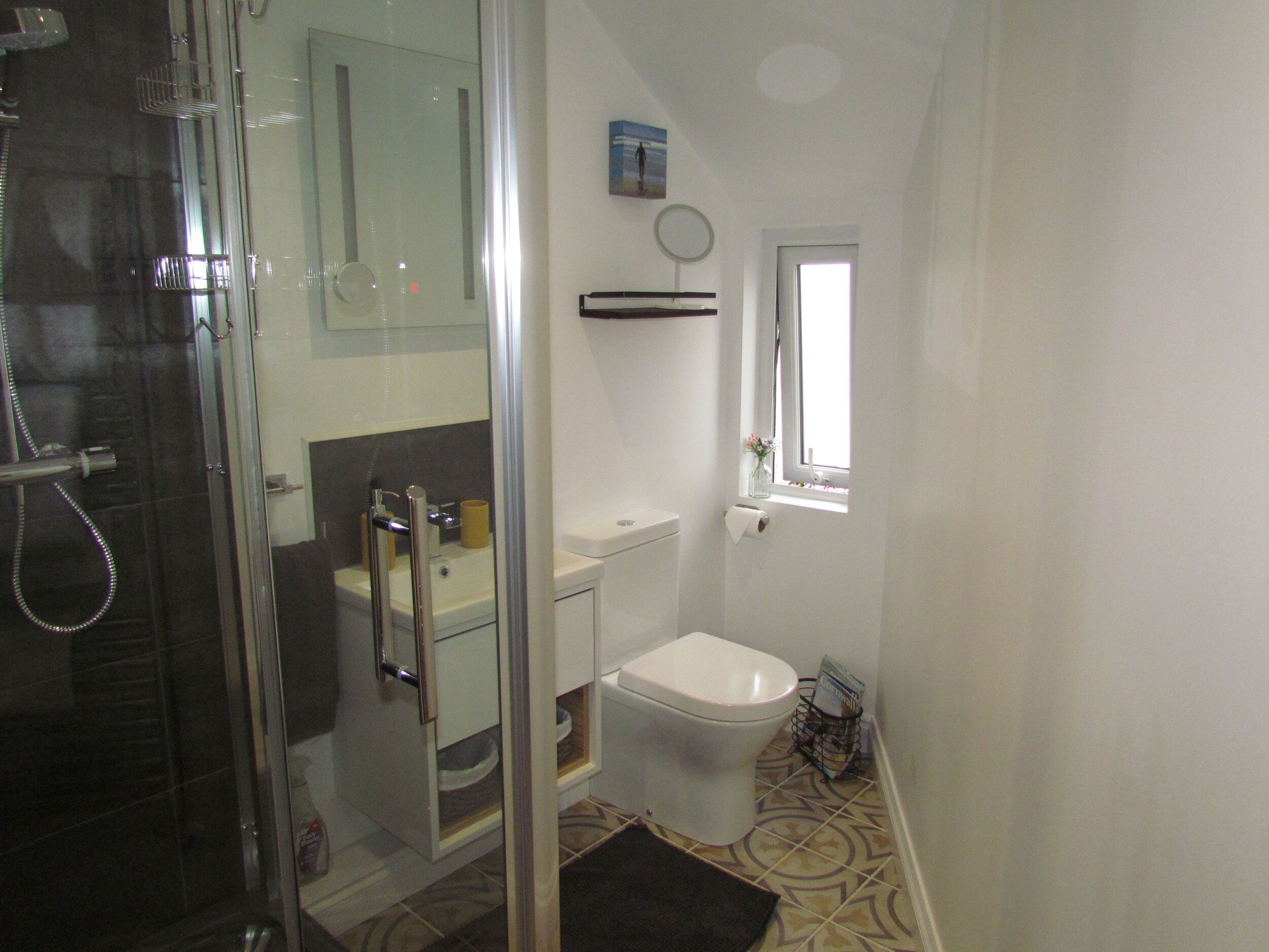 A bathroom with a glass shower enclosure, a toilet, a sink, and a small window.