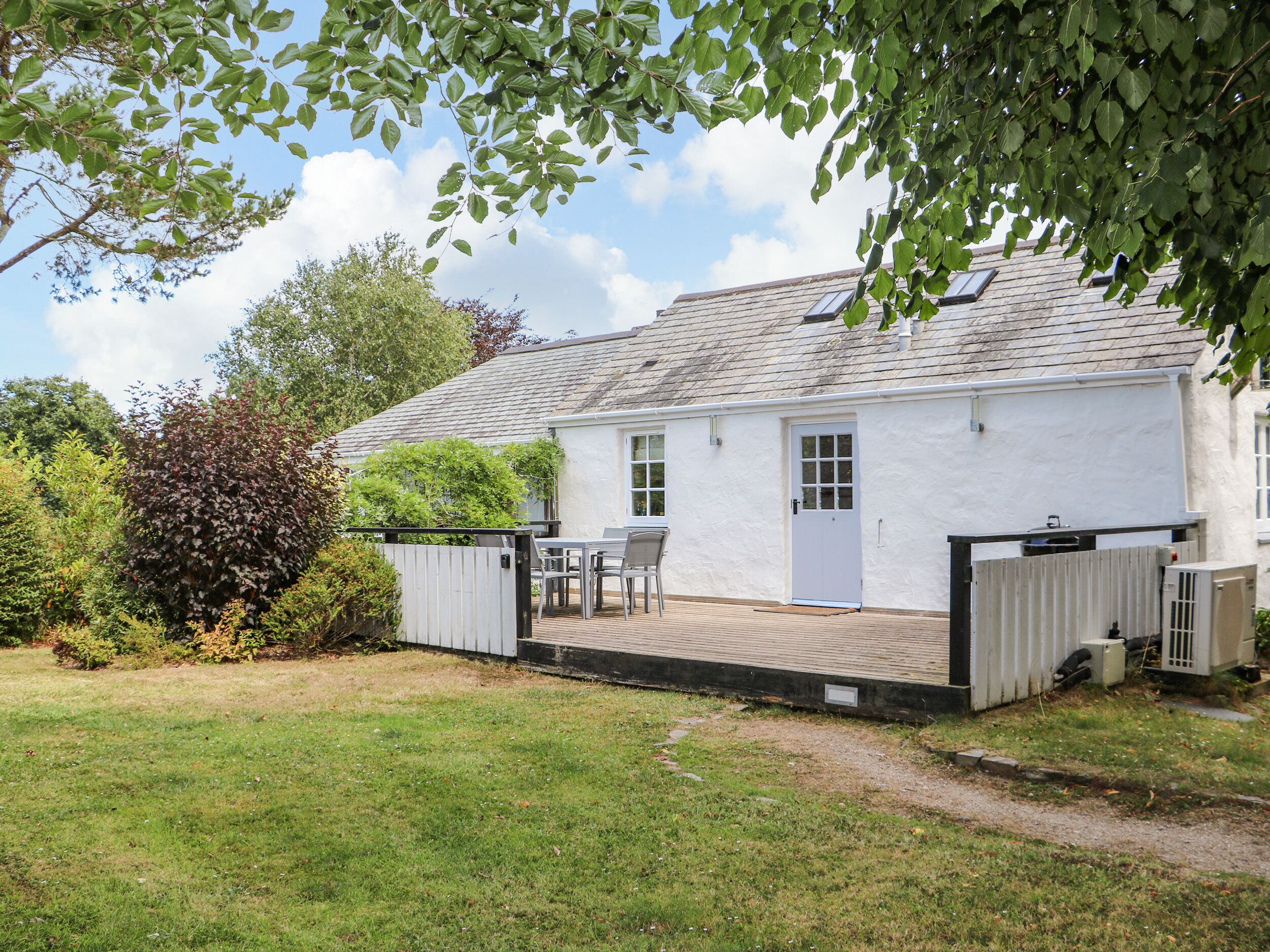 A white cottage with a tiled patio, a small table and chairs, and a fenced garden area.
