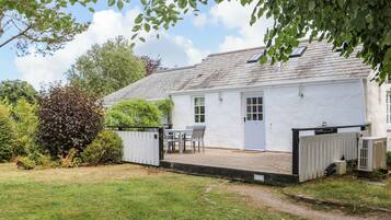 A white cottage with a tiled patio, a small table and chairs, and a fenced garden area.