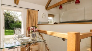 A modern kitchen with a glass dining table, wooden beams, and a view of the garden. - Little Chygowlin (Truro)
