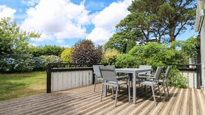 A wooden deck with a table and chairs, surrounded by a wooden fence and lush greenery. - Little Chygowlin (Truro)