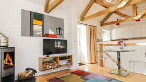 A modern living room with a fireplace, TV, wooden beams, and a colorful rug. - Little Chygowlin (Truro)