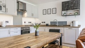 Cocina moderna con armarios blancos, encimera de madera y horno empotrado. Se observa una silla negra y un banco de madera.