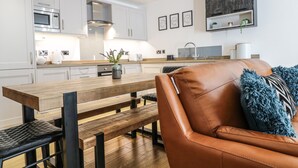 Una cocina moderna con armarios blancos, una mesa de comedor de madera y un sofá de cuero con un cojín azul.