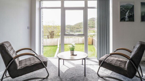 Una habitación con dos sillones tapizados, una mesita y un ventanal con vistas a un jardín y colinas.