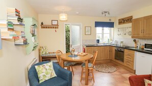 A cozy kitchen with wooden cabinets, a dining table, and chairs. There is a bookshelf with books and a small plant on the wall. - The Garden Lodge (Bridgnorth)