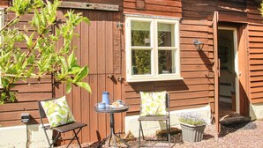 A wooden building with a window, a door, and a small table with chairs. - The Garden Lodge (Bridgnorth)