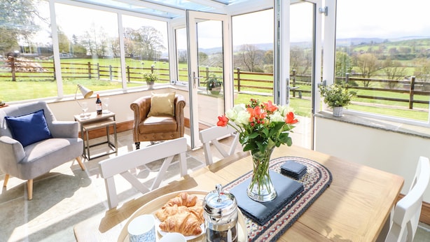 A bright room with large windows, a wooden table with a vase of flowers, a plate of croissants, and a coffee pot. - West Reins (Barnard Castle)