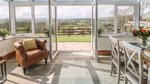 A conservatory with a view of a rural landscape, a leather sofa, and a dining table with chairs. - West Reins (Barnard Castle)
