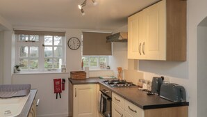 A compact kitchen with white cabinets, a stove, a toaster, and a clock on the wall. - Chestnut Cottage (Scarborough)