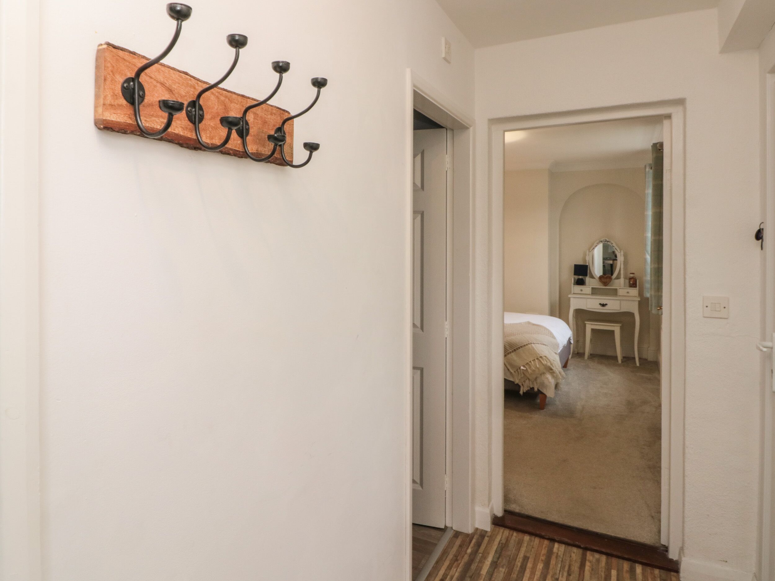 A hallway with a wooden coat rack and a door leading to a bedroom with a bed and a dresser.