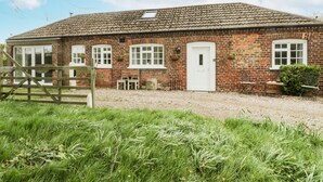 A brick house with a tiled roof, a white door, and a gravel driveway. - Chestnut Cottage (Scarborough)