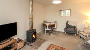 A living room with a wood-burning stove, a flat-screen TV, a dining table with chairs, a sofa, and a lamp. - Chestnut Cottage (Scarborough)