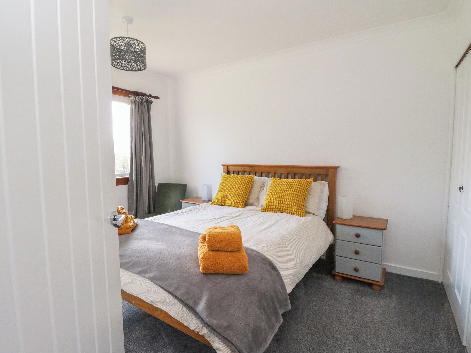 A bedroom with a bed, a nightstand, a chair, a lamp, and a window with curtains.