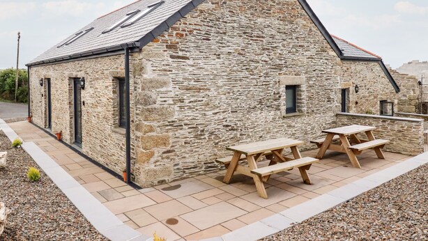 A stone building with a sloped roof, two wooden picnic tables, and a small window.