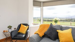 A modern living room with a large window, a black armchair, a grey sofa, and a small table with a plant and a cup. - Mynydd Mwyn (Llanfairpwllgwyngyll)