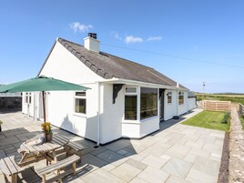 A white house with a tiled patio, a green umbrella, and a wooden table with flowers.