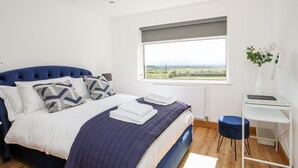 A bedroom with a bed, a window with a view, a bedside table, and a chair. - Mynydd Mwyn (Llanfairpwllgwyngyll)