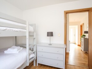 En køjeseng med hvidt sengetøj, et natbord med en lampe og trægulv.