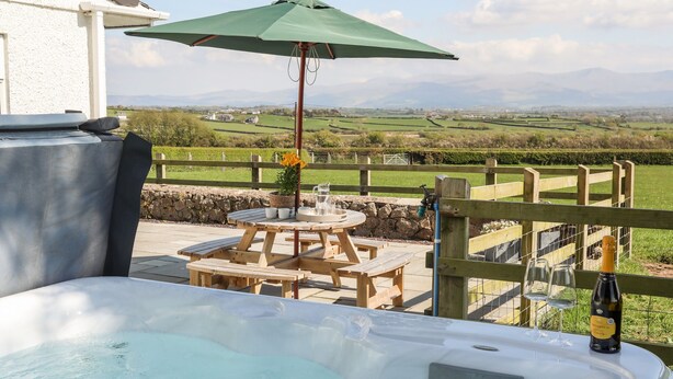 A hot tub with a wooden table and chairs, an umbrella, and a bottle of wine. - Mynydd Mwyn (Llanfairpwllgwyngyll)